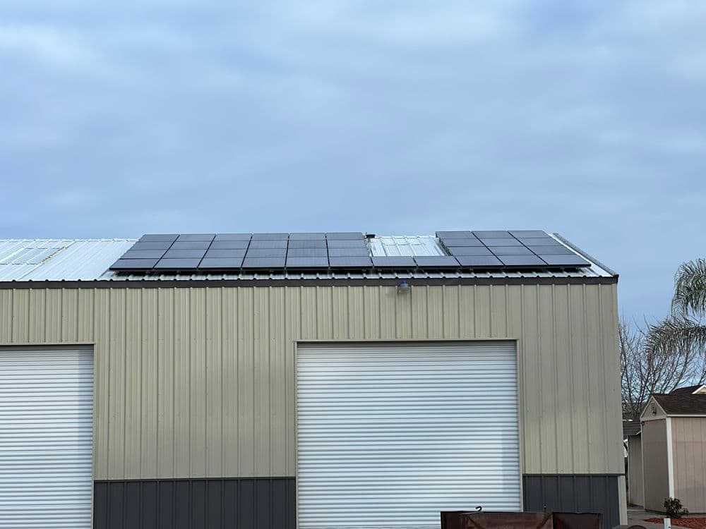 Solar panels installed on a metal building roof under a cloudy sky.