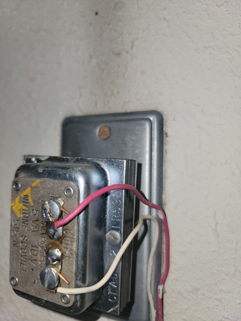 Close-up of a vintage electrical switch with exposed wiring on a textured wall.