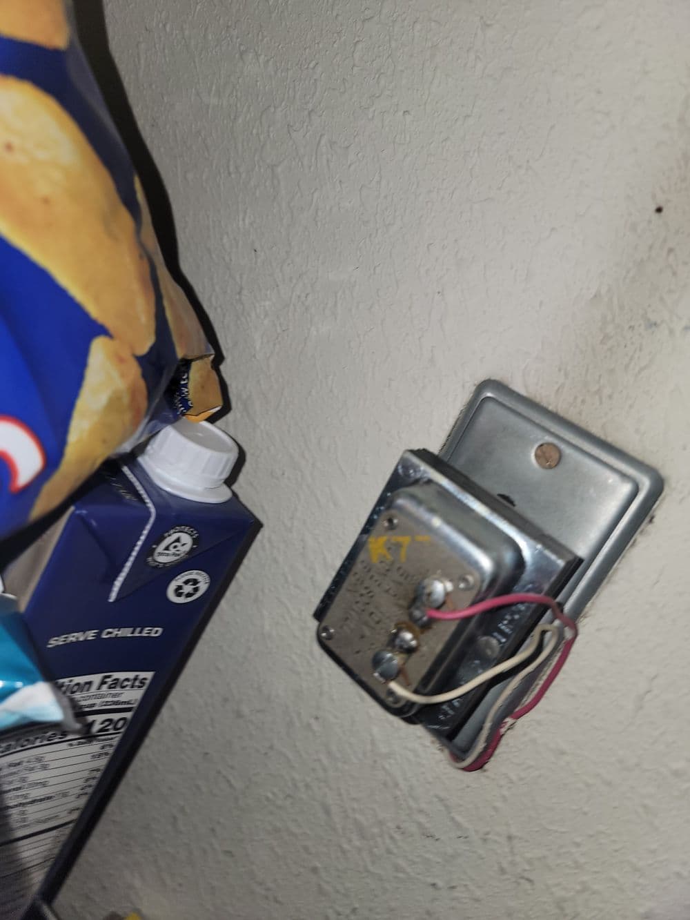 Electrical wall timer switch mounted on a beige wall with nearby food packaging.