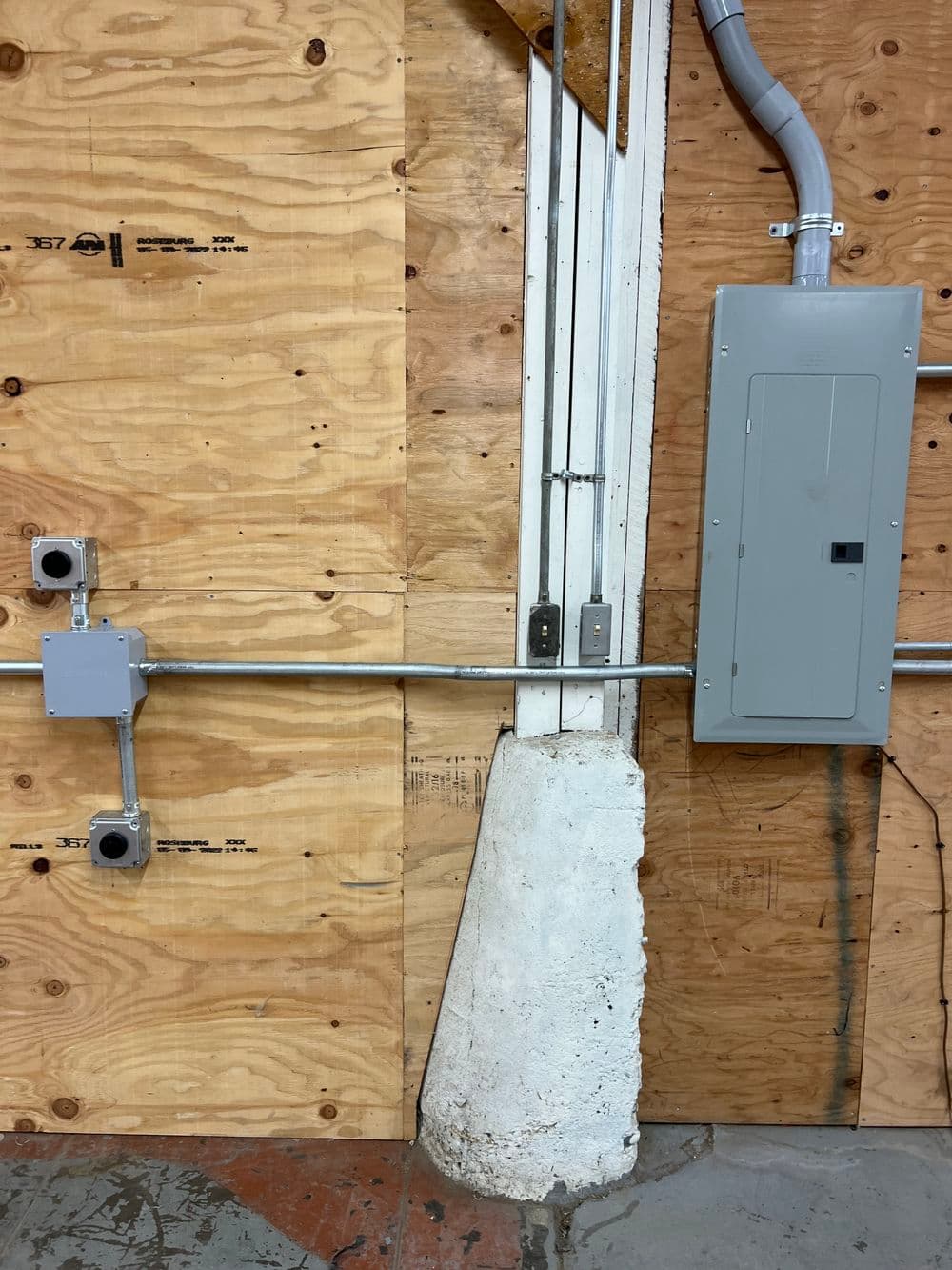 Electrical panel and conduit installation on wooden wall with concrete base.