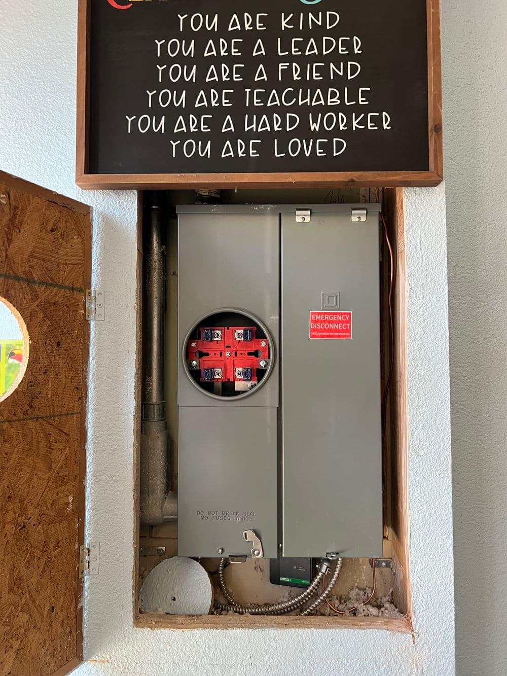 Electric panel installation behind a decorative wooden frame with motivational quotes.