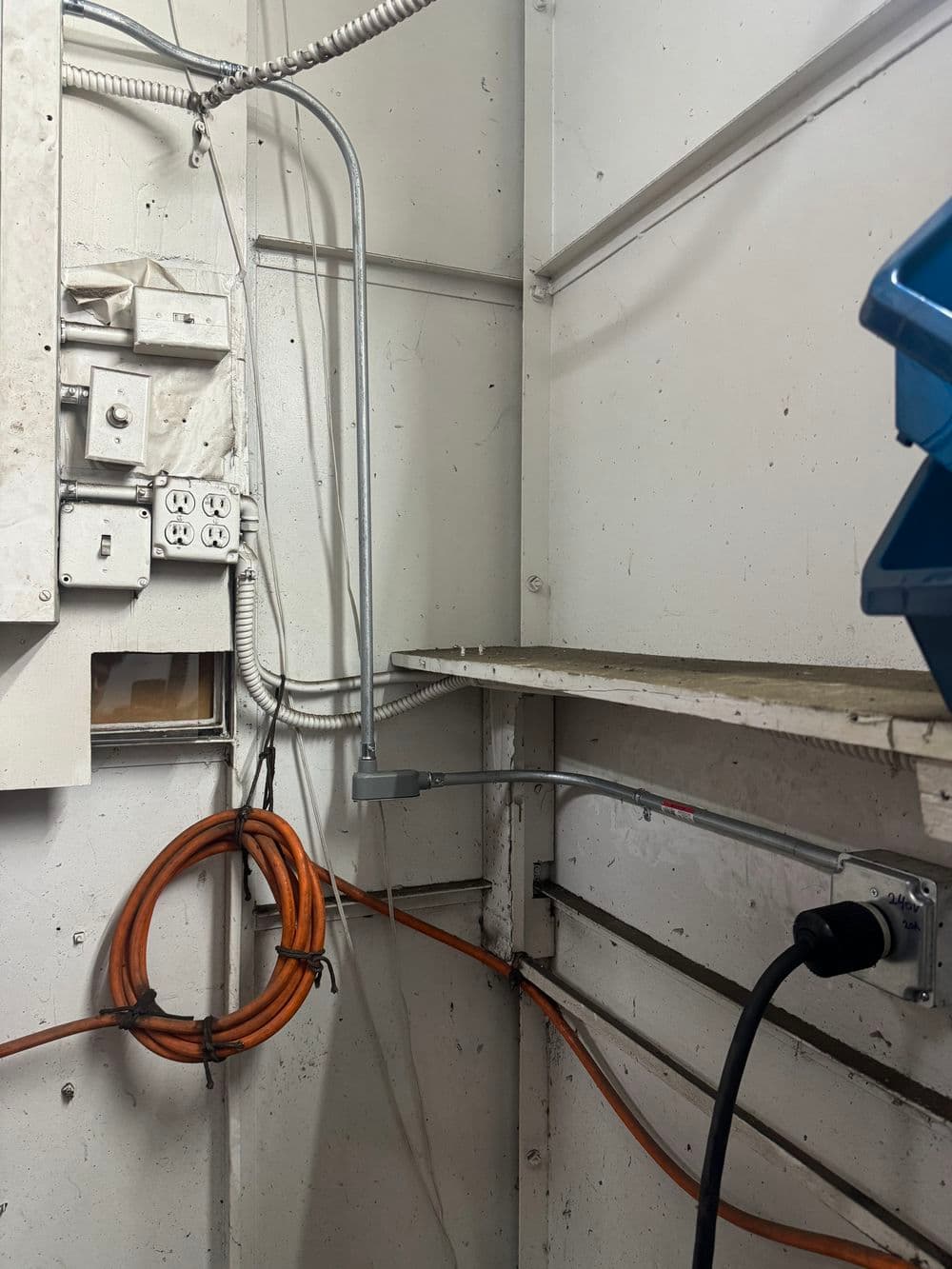 Electrical wiring and outlets in a utility room with hanging orange extension cord.