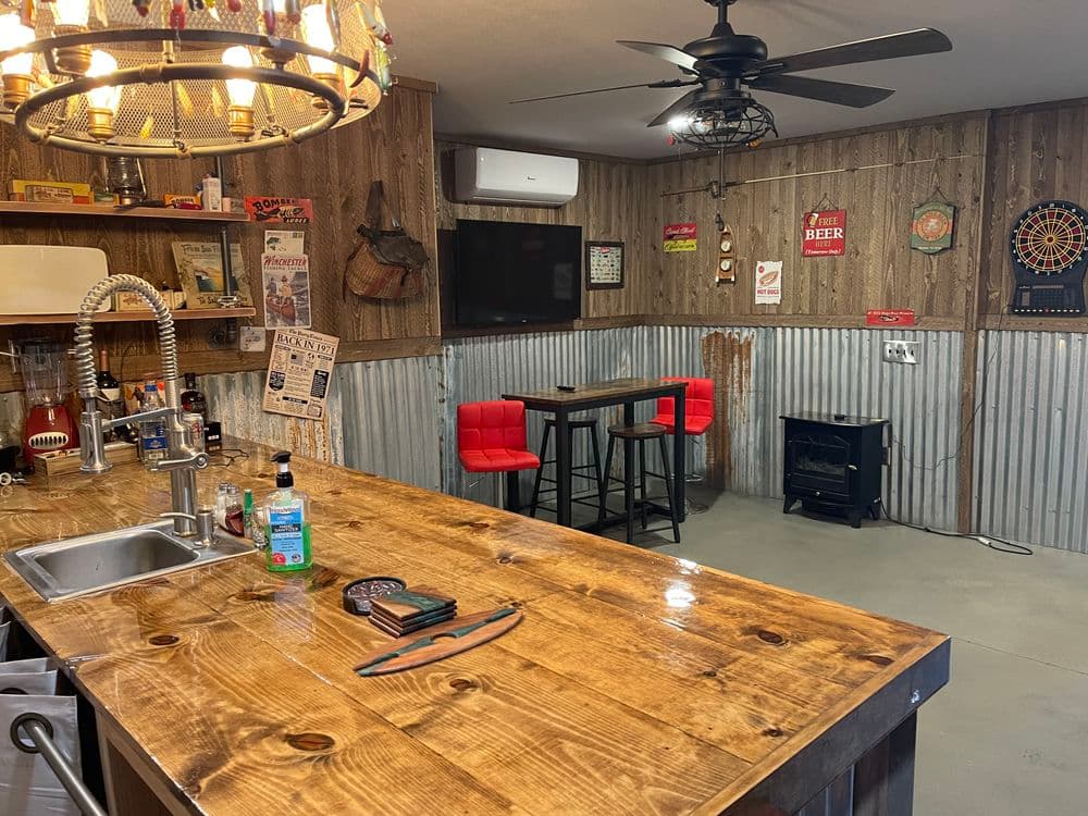 Cozy rustic bar area with wooden counter, red stools, and vintage decor on walls.