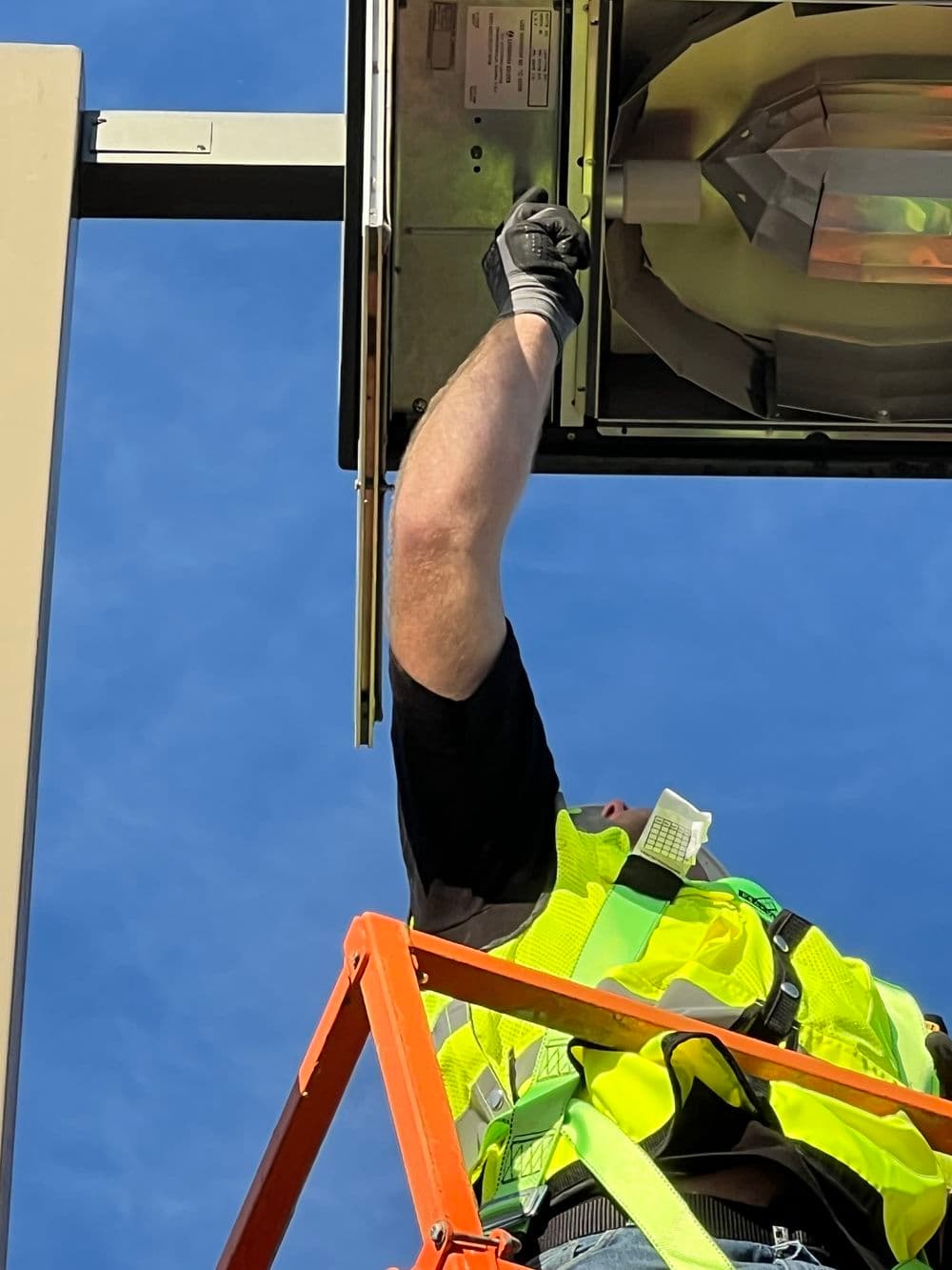 Electrician repairing streetlight while on ladder against clear blue sky. Safety gear visible.