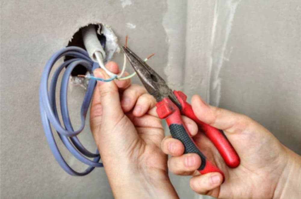 Person using pliers to fix electrical wires during home renovation. Safety precautions advised.