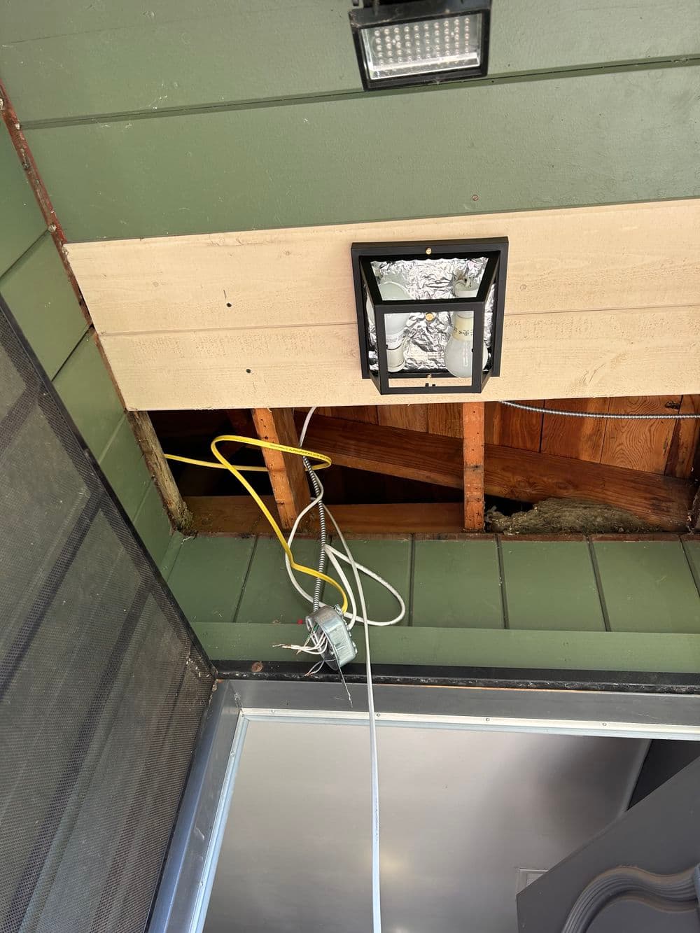exposed ceiling with light fixture wiring and wooden beams in a green wall setting