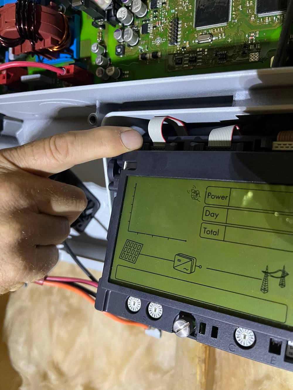 Technician pointing to a digital display on electronic equipment with circuit board visible.