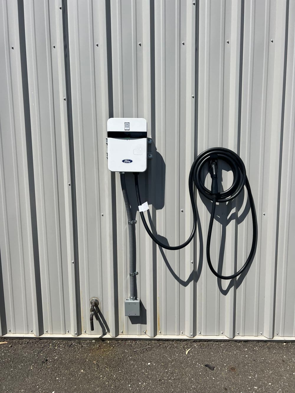 Electric vehicle charging station mounted on a metal wall with a coiled charging cable.