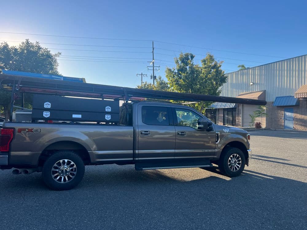 Brown pickup truck with a rack parked in a lot near a building and trees.